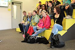 Erste Reihe auf der gelben Treppe mit aufmerksamen Zuhörern samt Blindenführhund