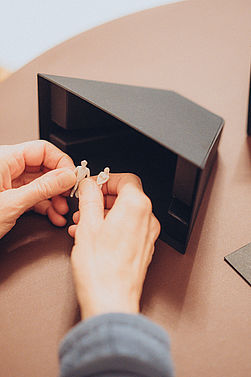 Bildtext: Zwei Hände bewegen Puppen in einer kleinen Bühne